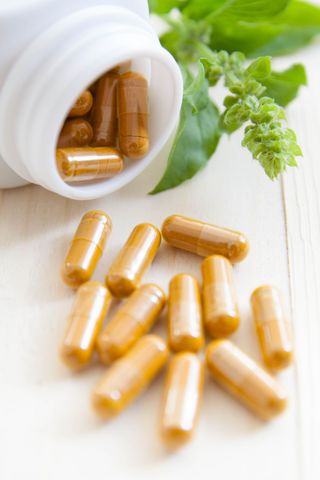 Orange capsules spilling from a white bottle, next to green leaves on a white surface.