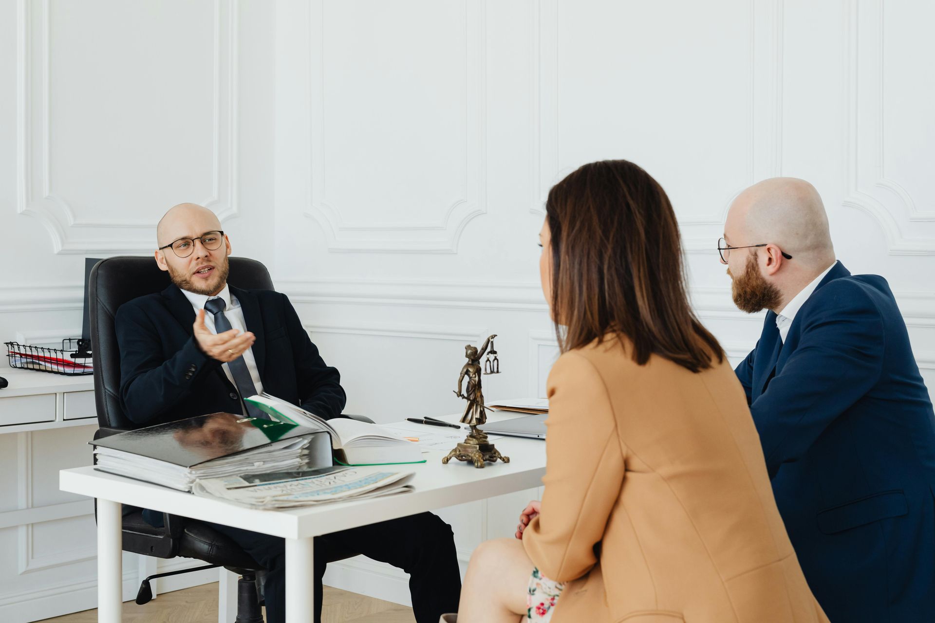 Three people in a bright office meeting, seated around a white table with papers and a small statue.