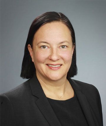 Studio headshot of a smiling person in a black blazer against a gray background
