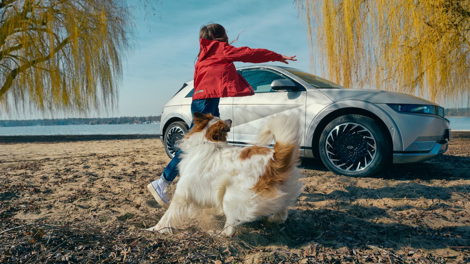 A woman is playing with a dog on the beach next to a car. ioniq 5