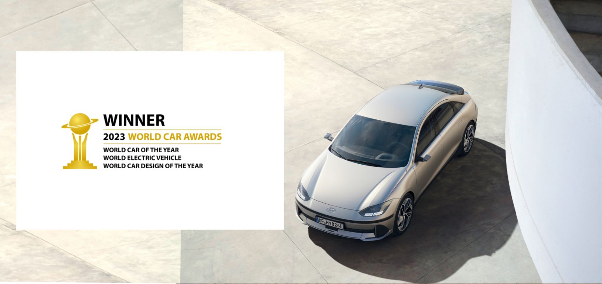 A white car is sitting on a concrete surface next to a winner 's trophy. Ioniq 6
