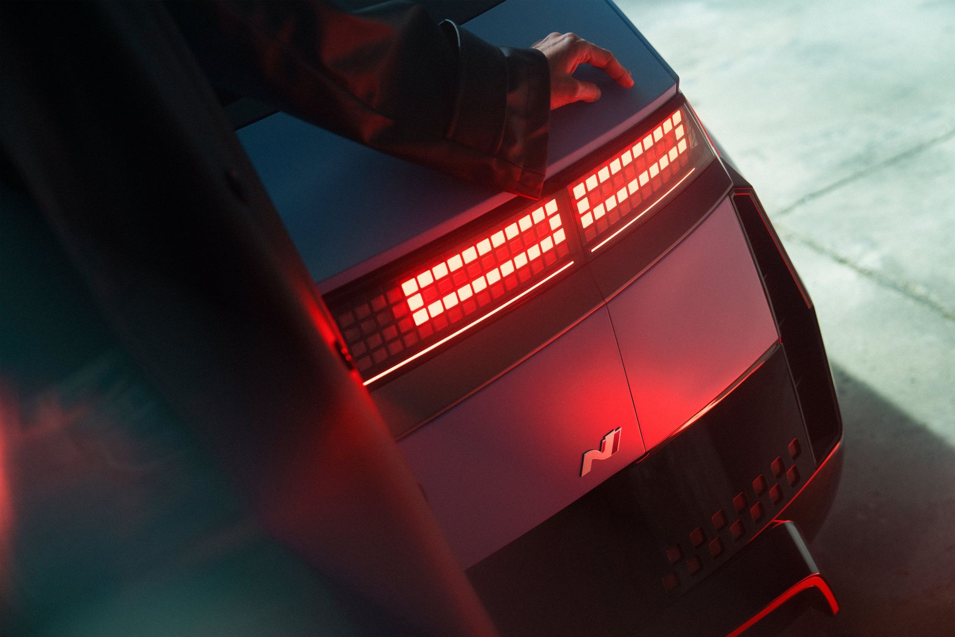 A person is standing next to a car with a red tail light. Ioniq 5 N
