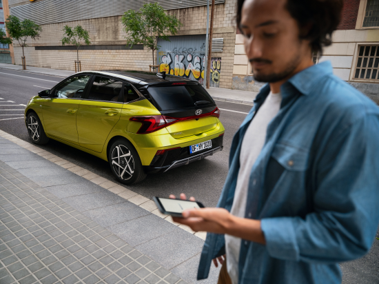 A man is holding a tablet in front of a yellow car. i20