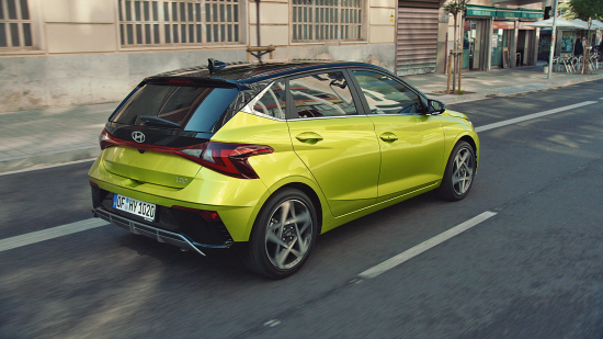 A green car is driving down a city street. i20