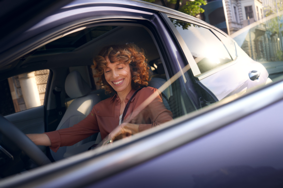 A woman is sitting in the driver 's seat of a car. Kona Electric