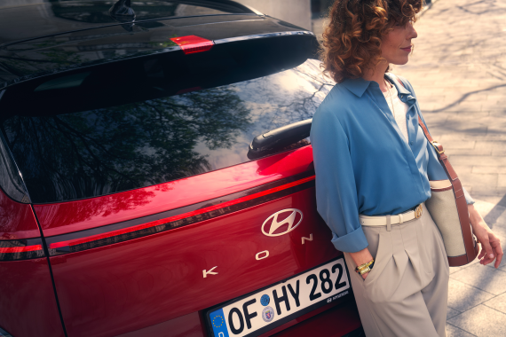 A woman is standing next to a red hyundai car.