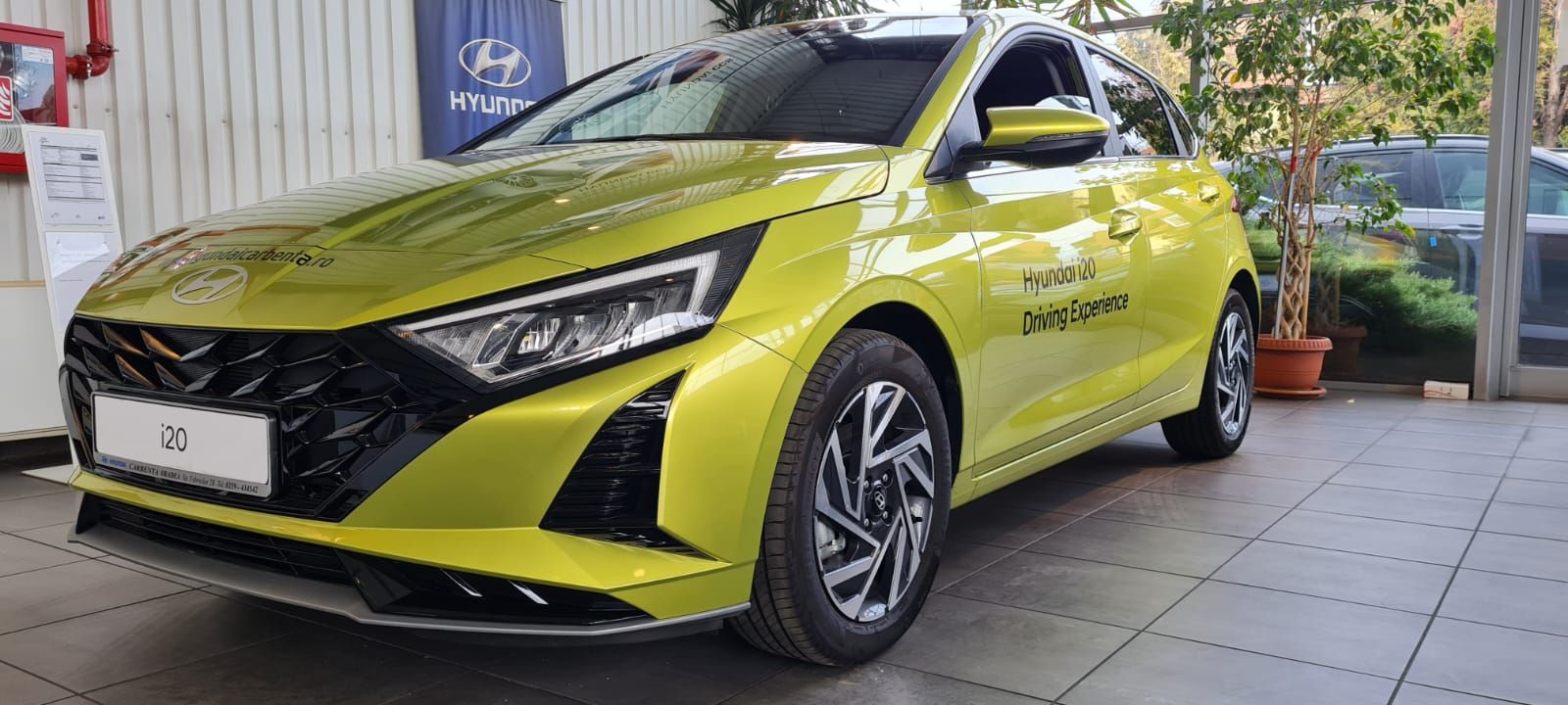 A yellow hyundai i20 is parked in a showroom.