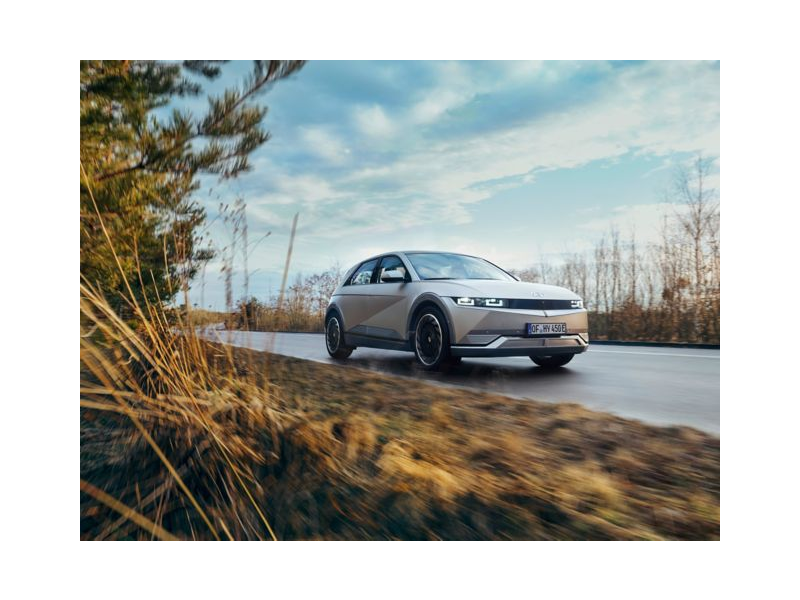 A white car is driving down a road next to a field. Ioniq5