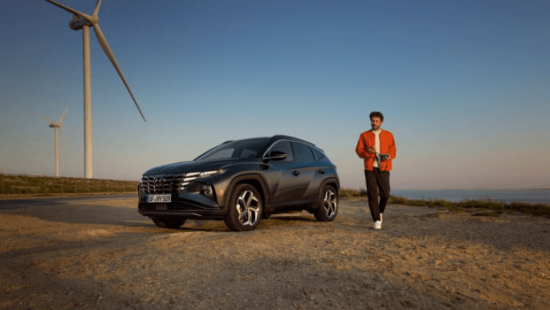 A man is standing next to a car in front of a wind turbine. Tucson