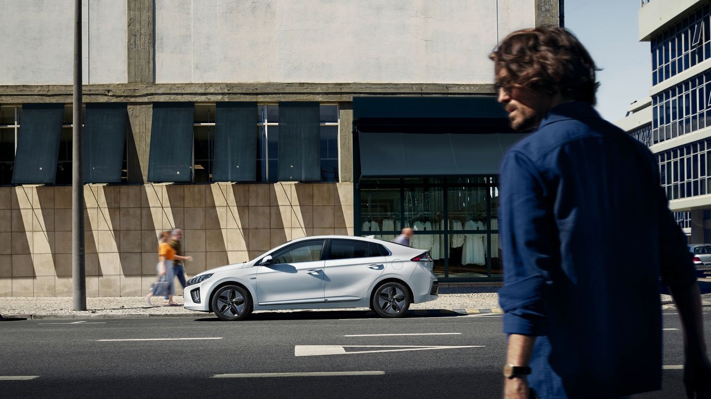 A man is walking down the street next to a white car.