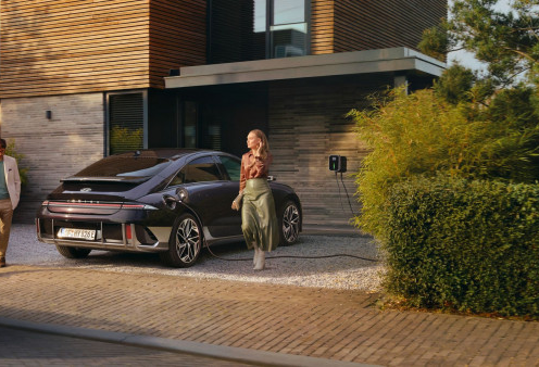 A woman is walking towards a car that is parked in front of a house.