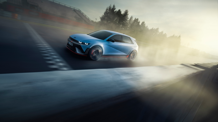 A blue car is driving down a road with trees in the background. Ioniq 5 N