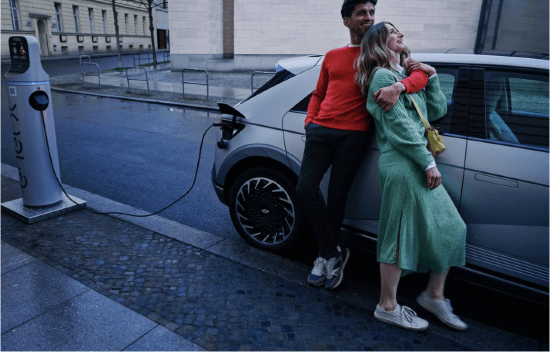 A man and a woman are standing next to a car that is being charged.