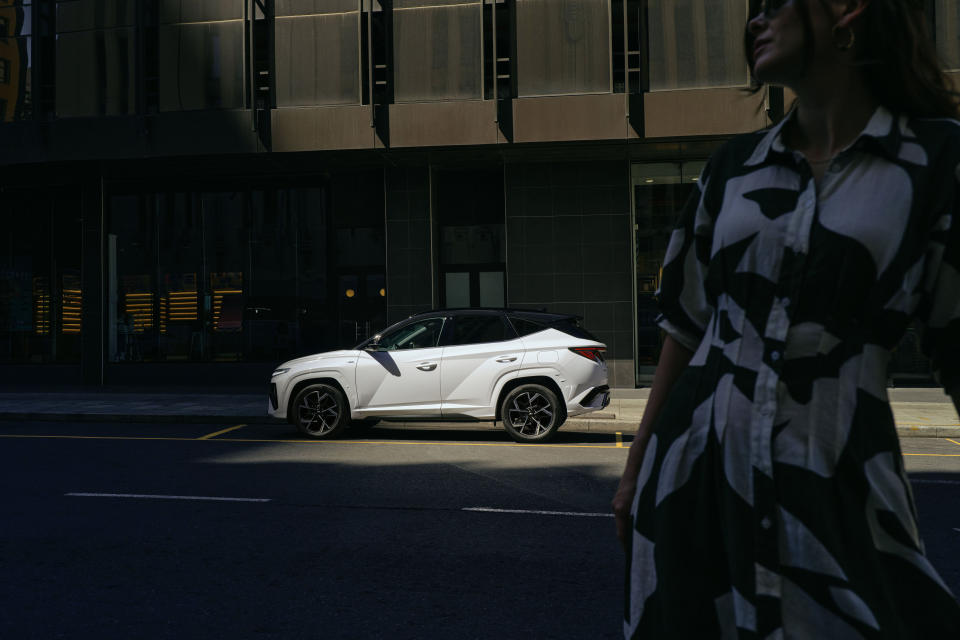 A woman is walking down the street in front of a white car.