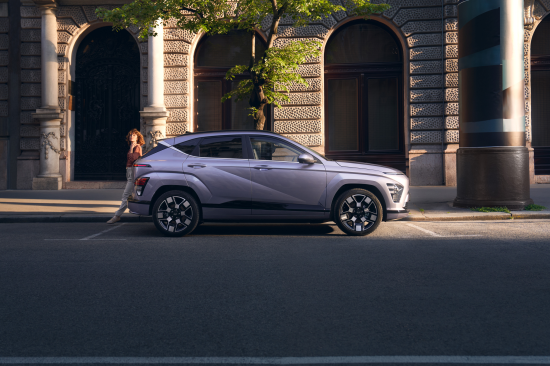 A silver car is parked on the side of the road in front of a building. Kona Electric