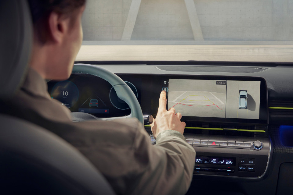 A man is driving a car and pressing a button on the dashboard. Kona