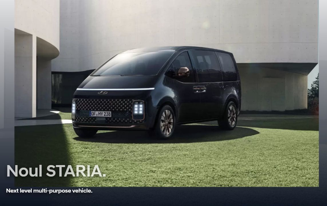 A black van is parked in front of a building. Staria