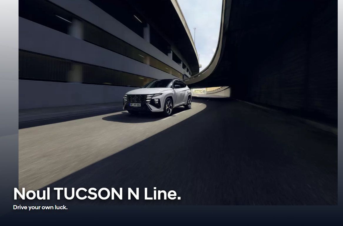 A white car is driving down a road next to a building.
