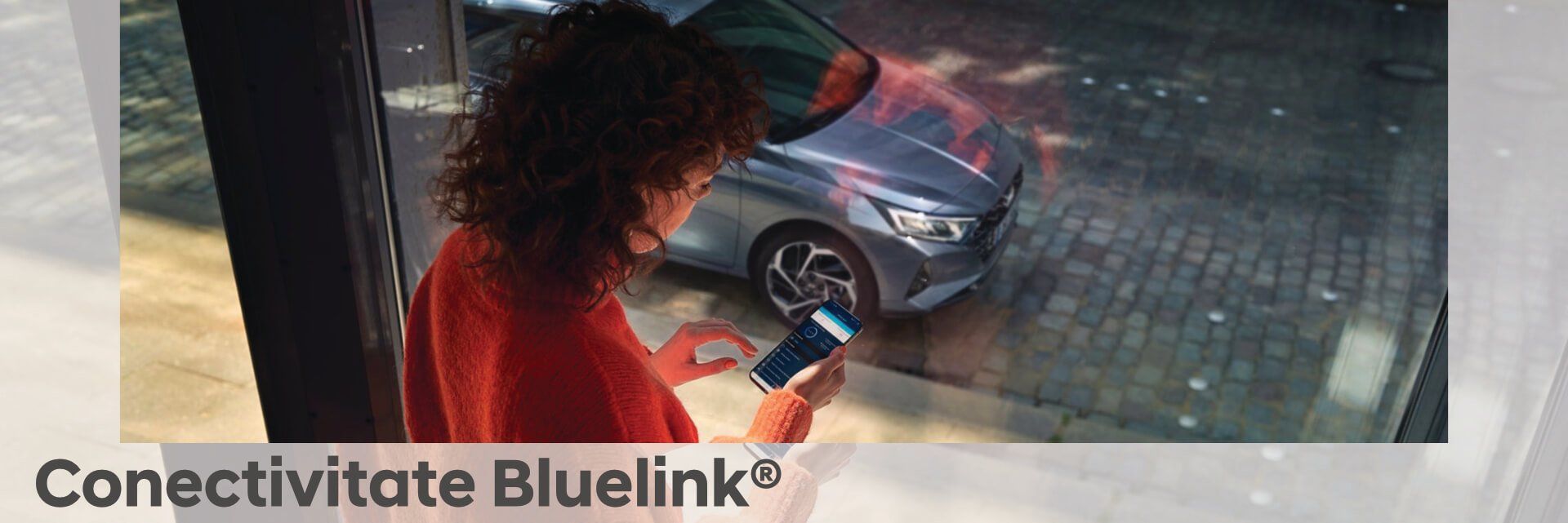A woman is looking at her phone in front of a car.