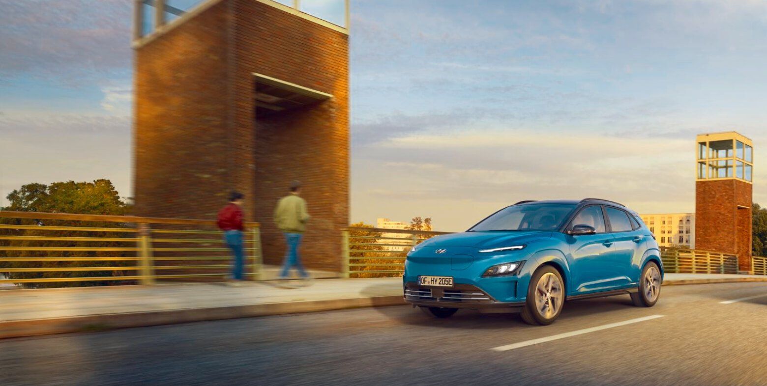 A blue car is driving down a street next to a brick building.