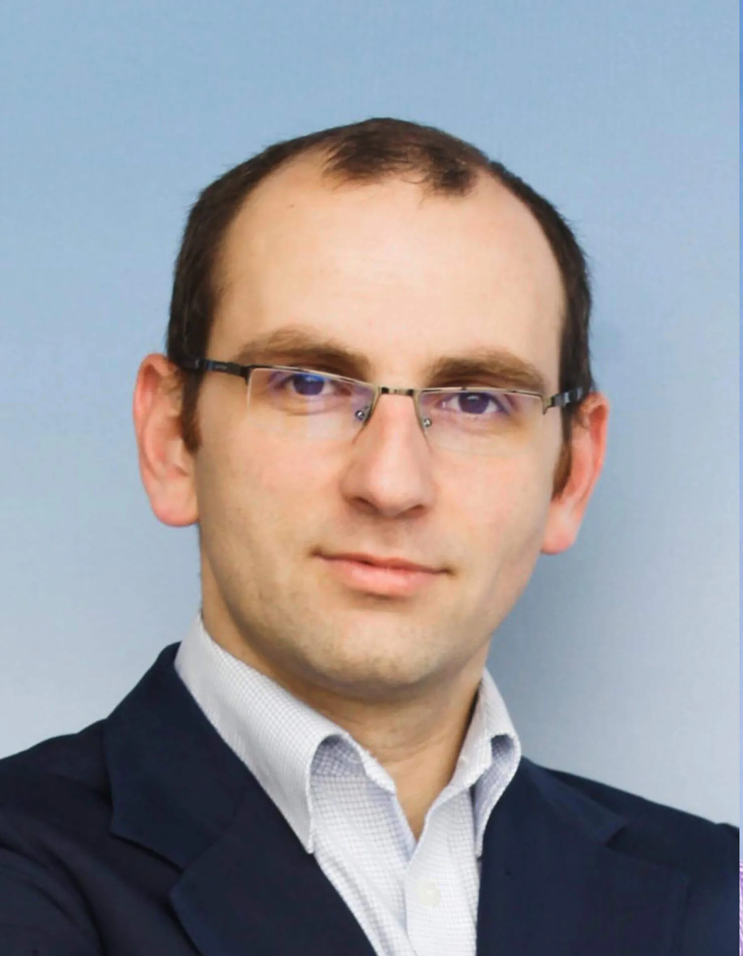 A man wearing glasses and a suit looks at the camera