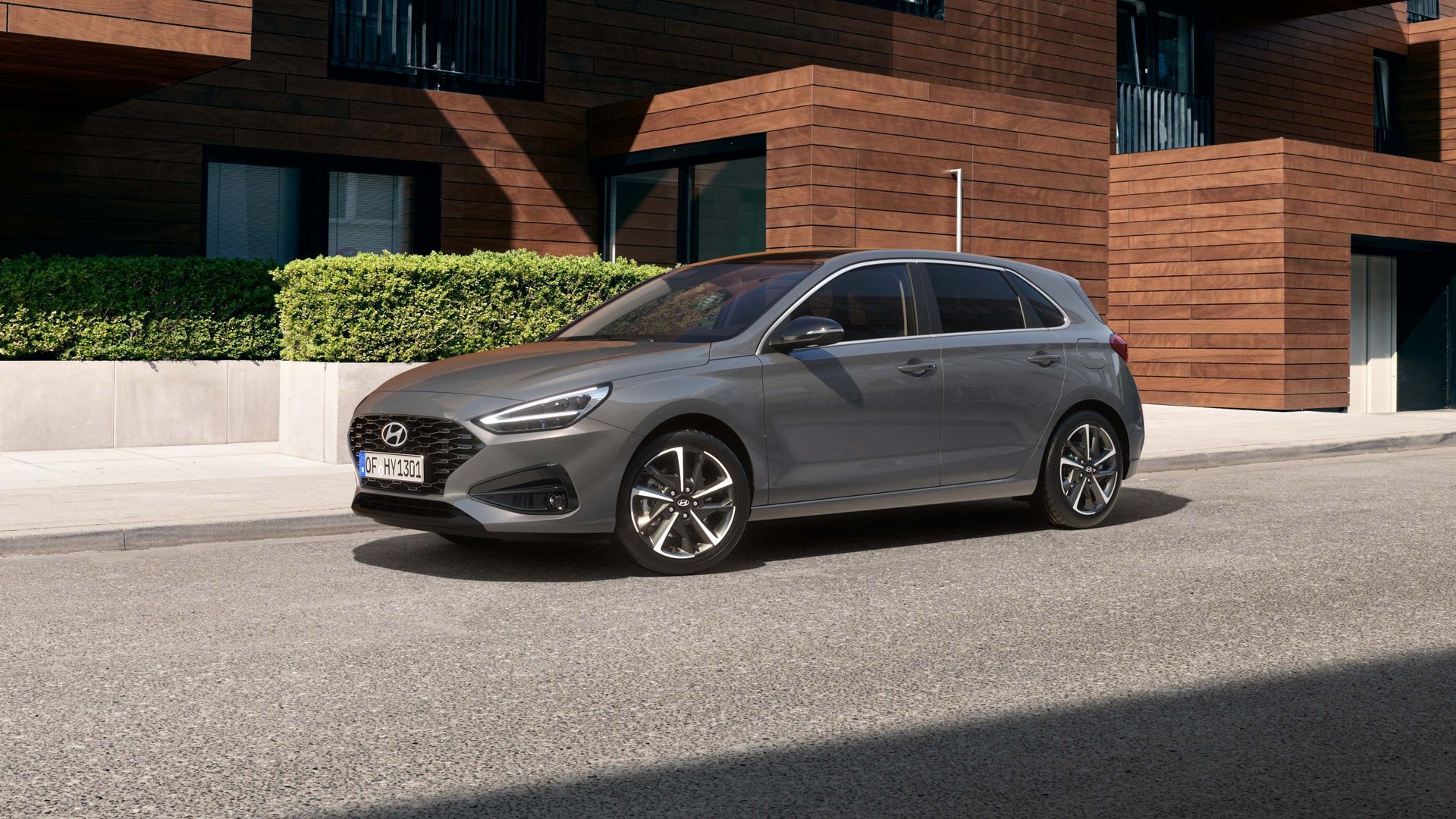 A gray car is parked on the side of the road in front of a brick building. i30 wagon