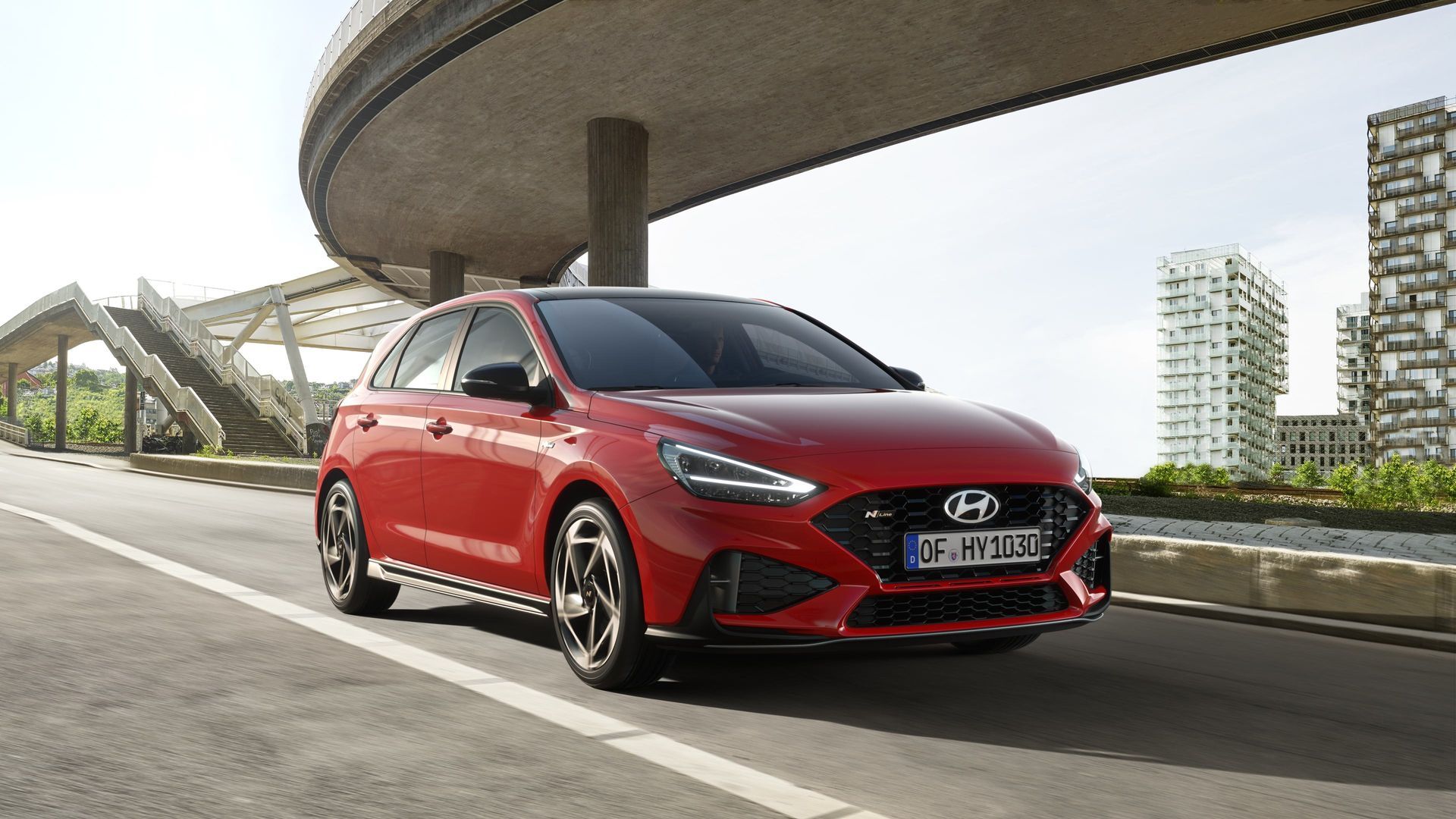 A red hyundai i30 is parked on the side of the road under a bridge.