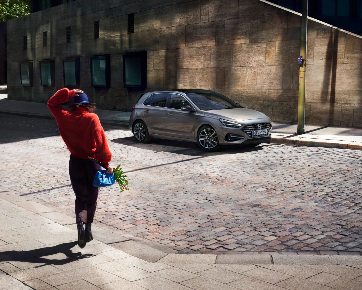 A woman is walking down a cobblestone street next to a car. i30