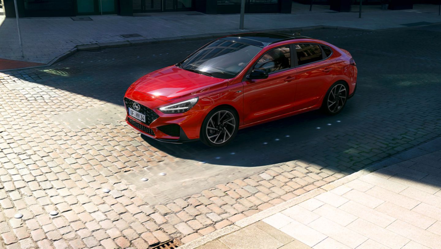 A red car is parked on a cobblestone street. i30
