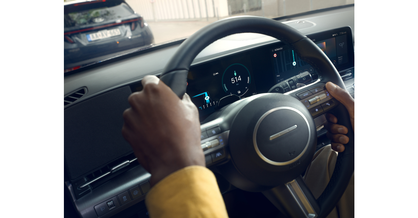 A person is holding a steering wheel in a car. Kona Electric