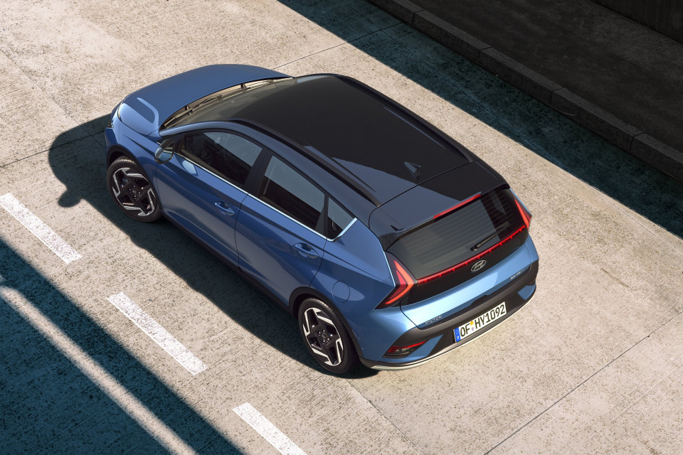 A blue car with a black roof is parked on the side of the road. Bayon