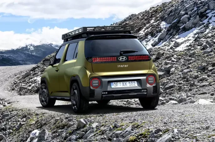 A yellow car with a roof rack is driving down a rocky road. Inster
