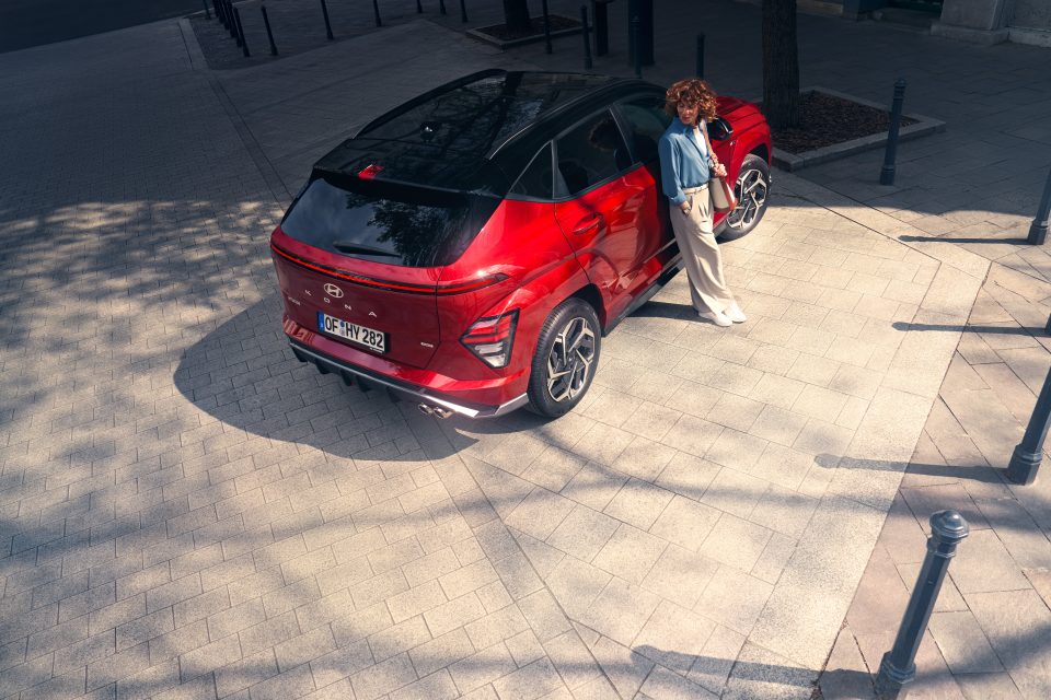 A woman is standing next to a red car on a sidewalk.