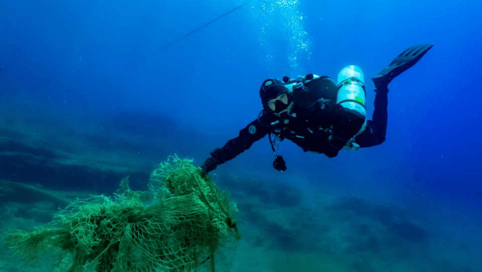 A scuba diver is swimming in the ocean near a rock.
