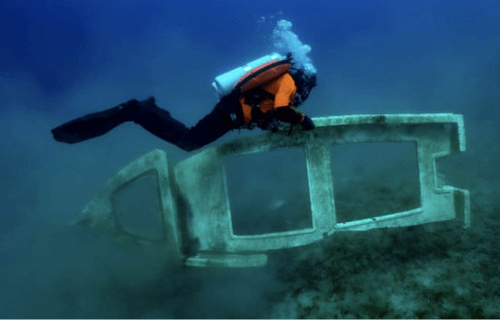 A scuba diver is swimming over a concrete structure in the ocean