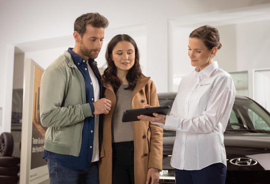 A man and a woman are looking at a tablet in a car showroom. v