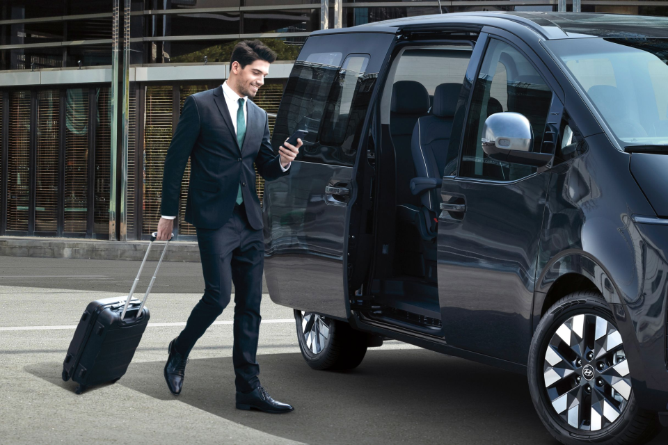 A man in a suit is pulling a suitcase into a van. Staria