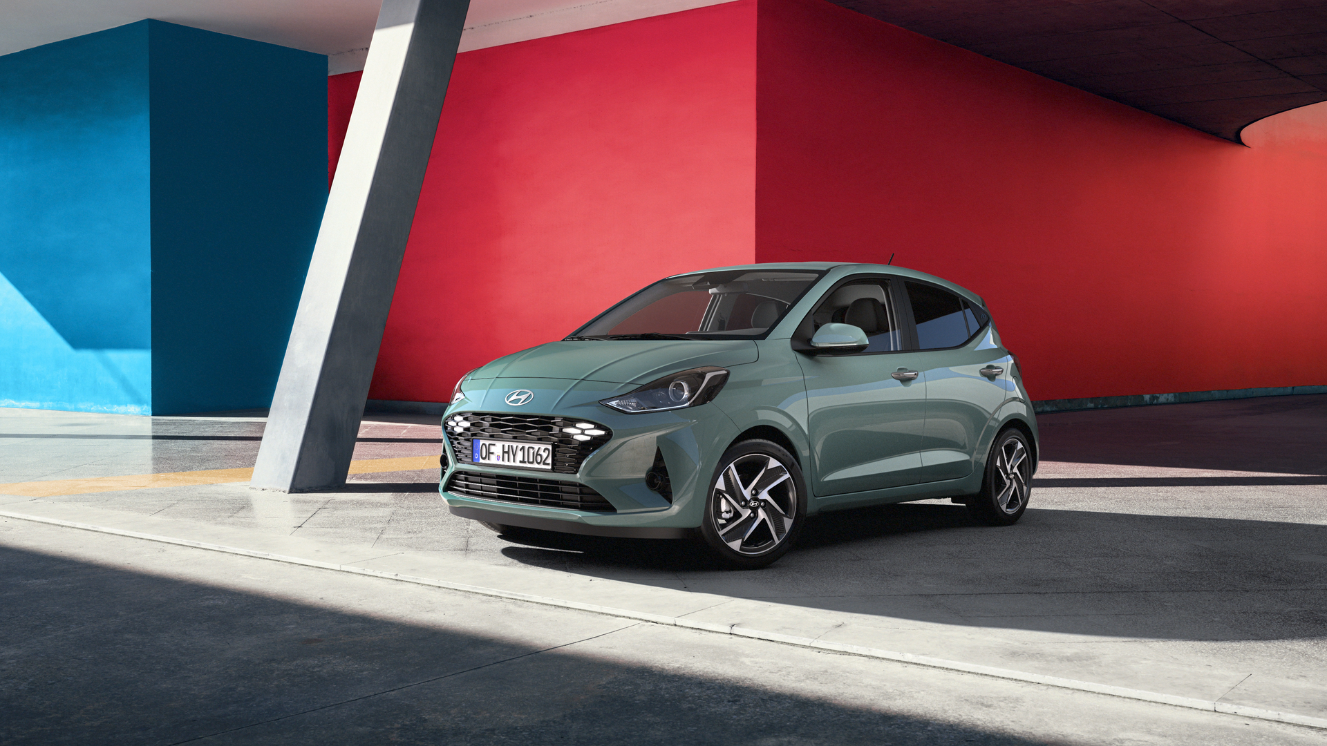 A green car is parked in front of a red and blue building.