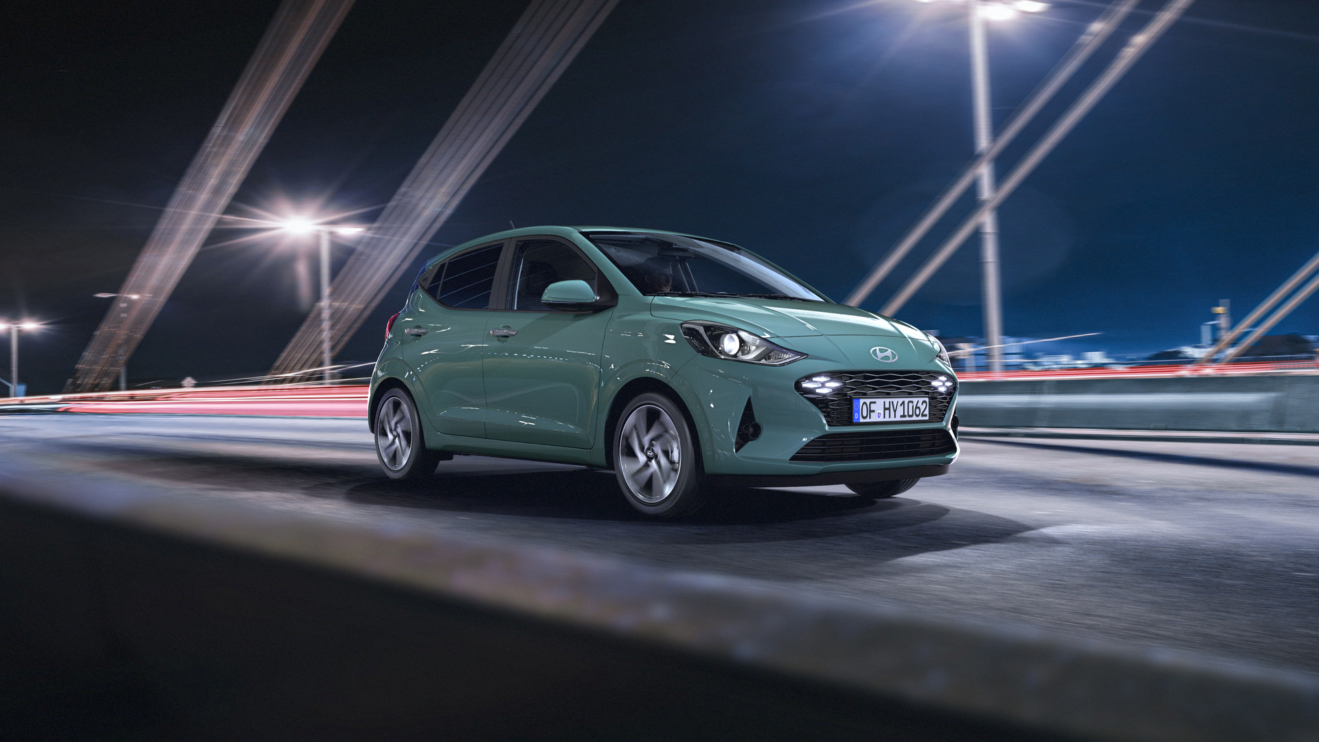 A green car is driving on a bridge at night. i10