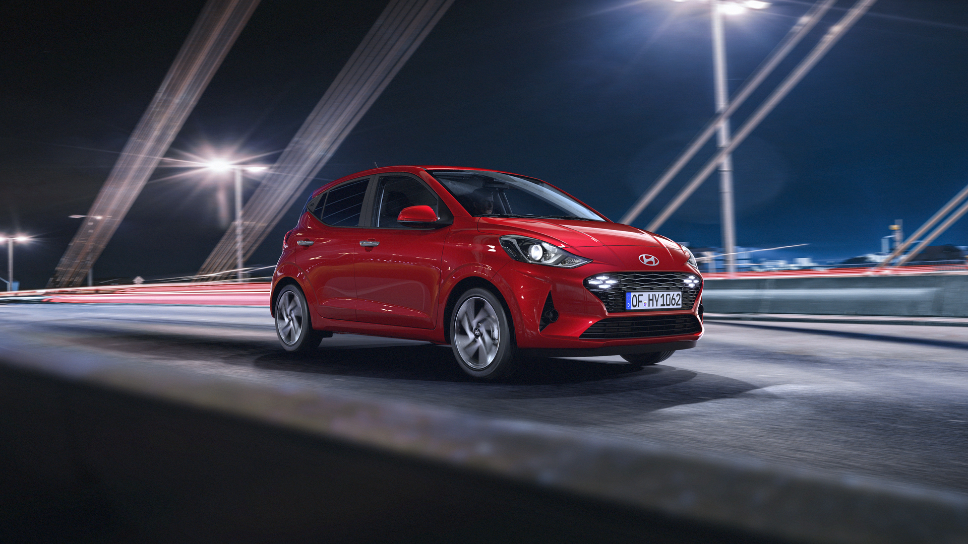 A red car is driving on a bridge at night. i10