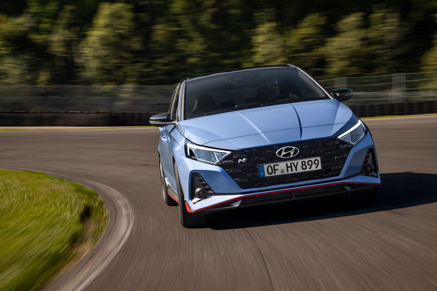 A blue hyundai i20 n is driving down a curvy road. i20 N