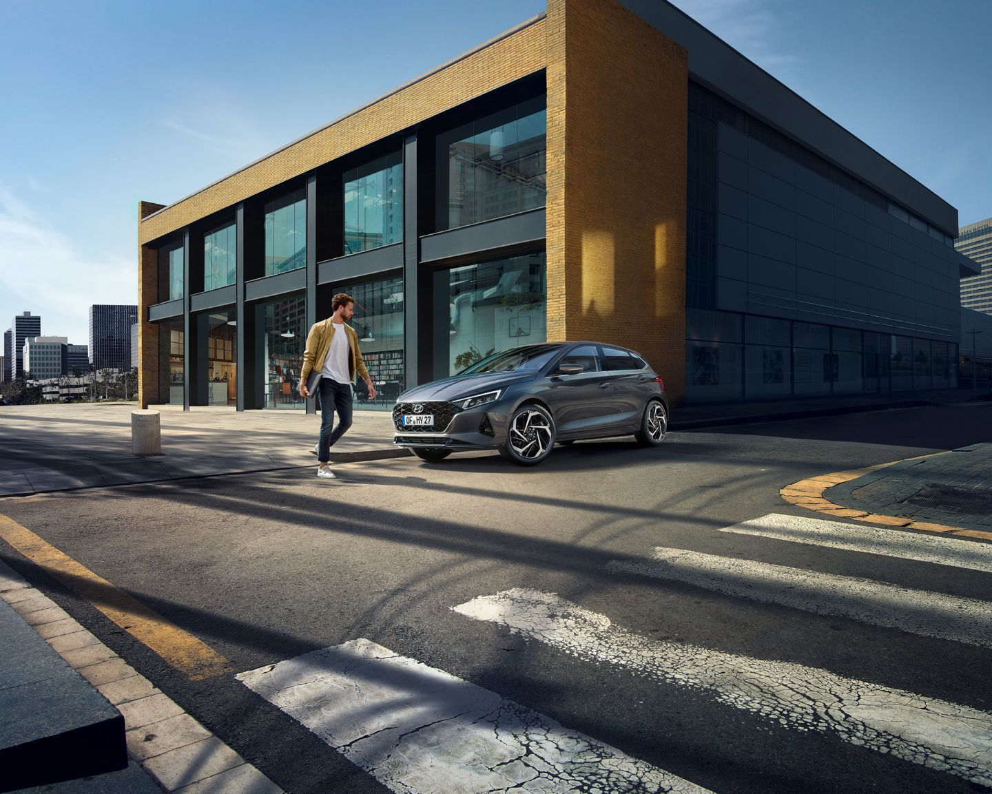A man is crossing the street in front of a building next to a car. i20