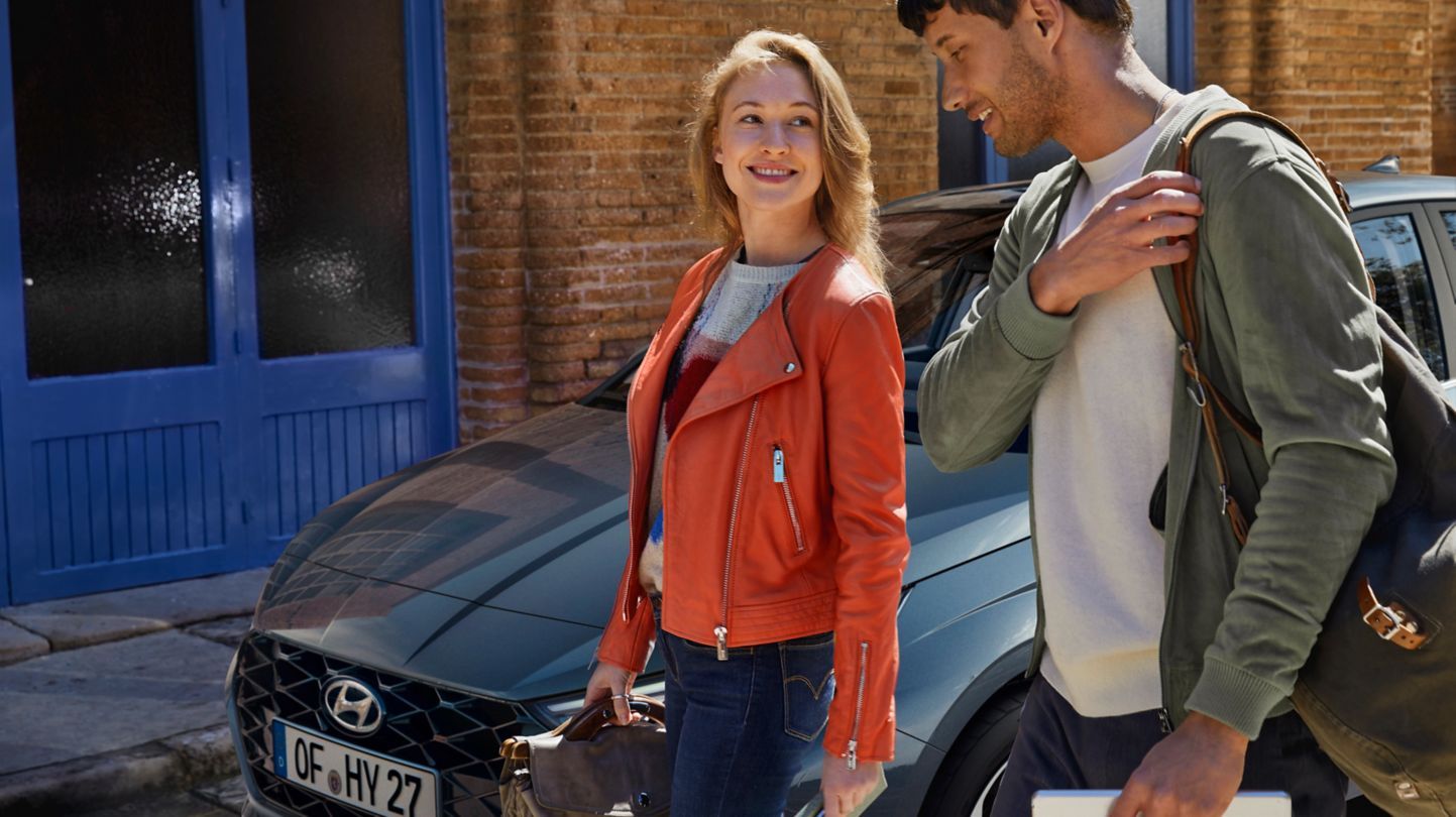 A man and a woman are standing next to a car. i20