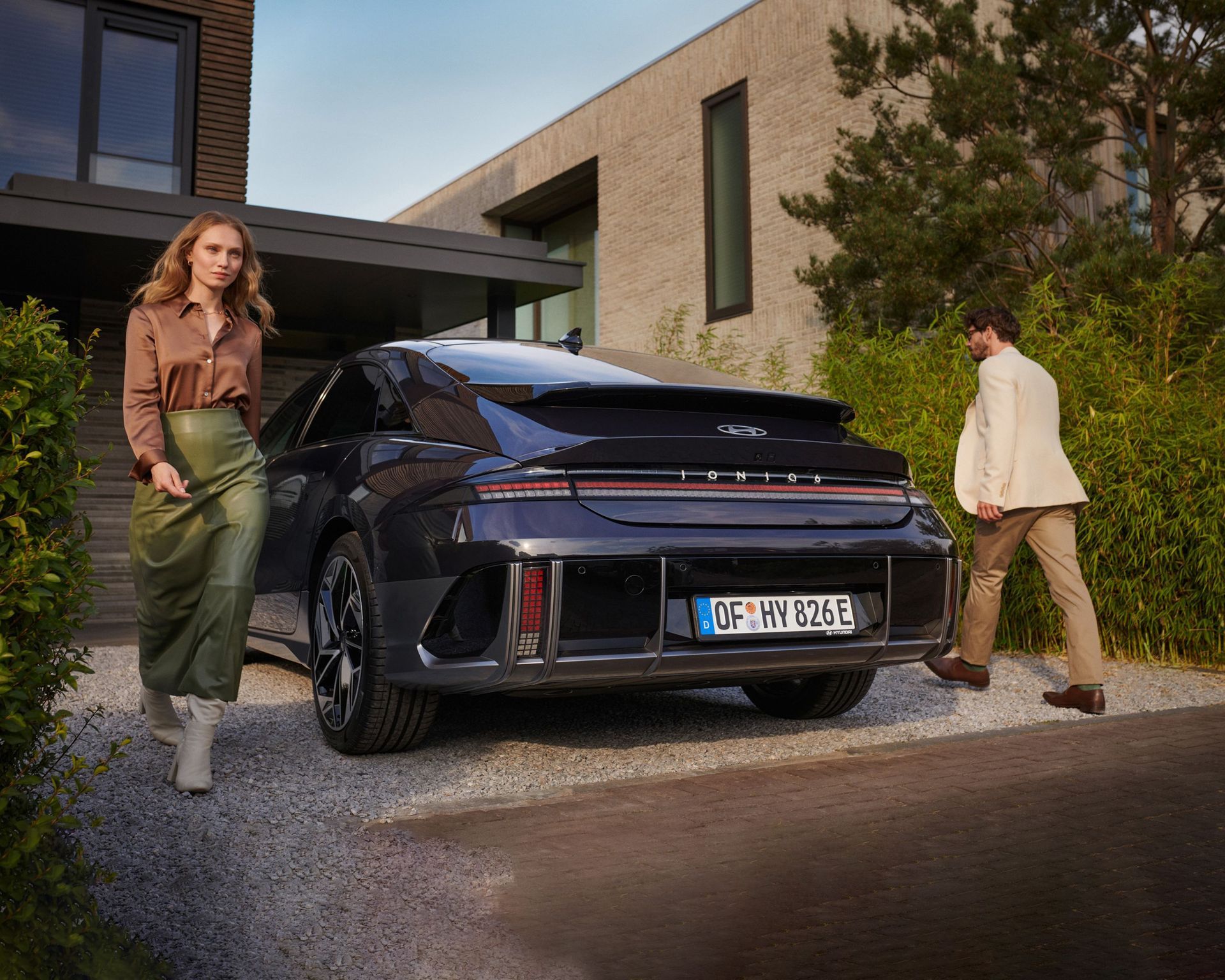 A man and a woman are standing next to a car parked in front of a house. Ioniq 6