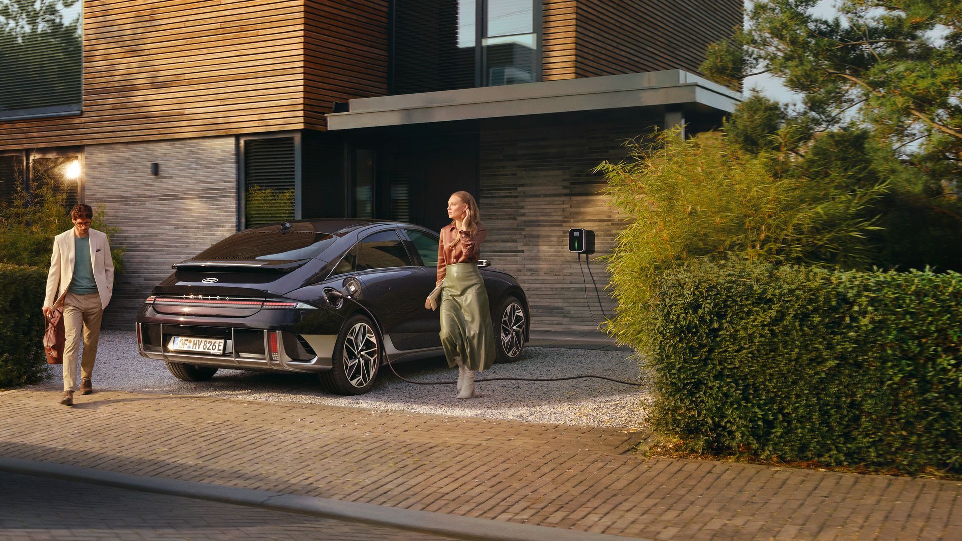 A woman is walking towards a car parked in front of a house. Ioniq 6