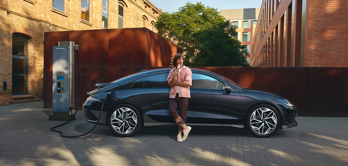 A woman is standing next to an electric car that is being charged. Ioniq 6