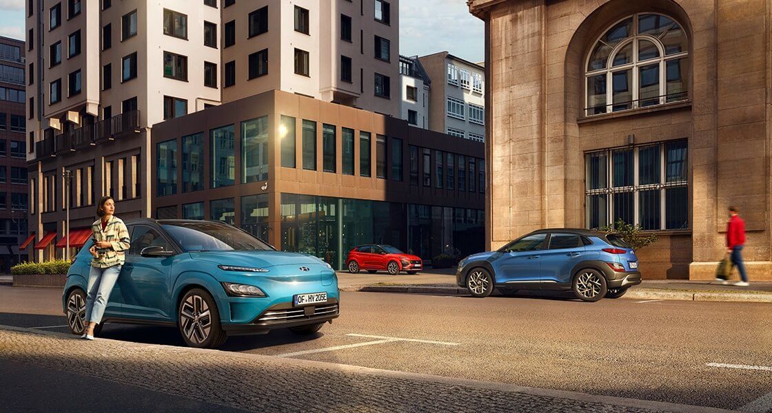 A man is standing next to a blue car on a city street.