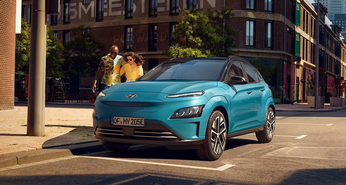 A blue electric car is parked on the side of a city street.