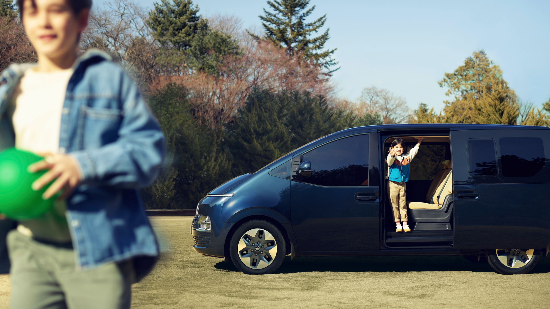 A boy is holding a green ball in front of a van. Staria