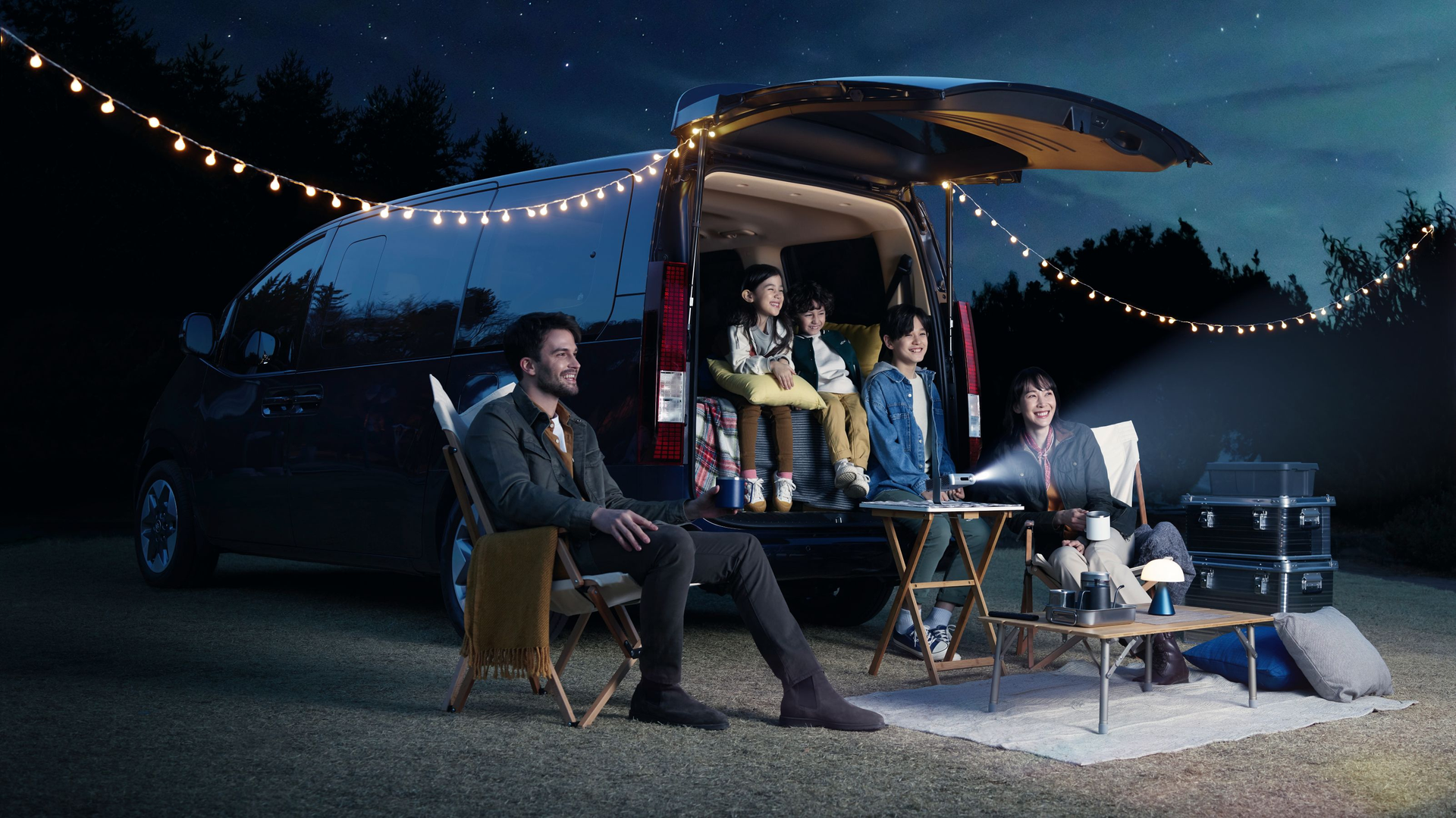 A group of people are sitting in the back of a van at night. Staria